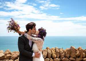 wedding couple kissing in front of dry stone wall overlooking sea