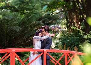 Photo by Lizzy Morris married couple standing on a red bridge at abbotsbury subtropical gardens